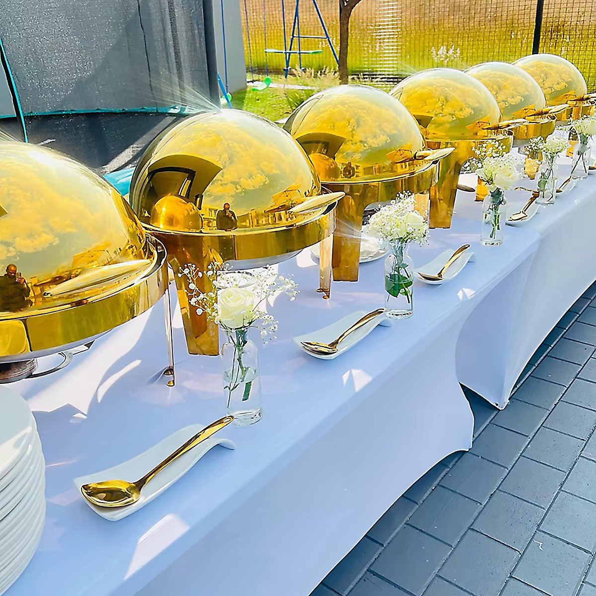 Gold buffet serving dishes on an outdoor event table with white flowers